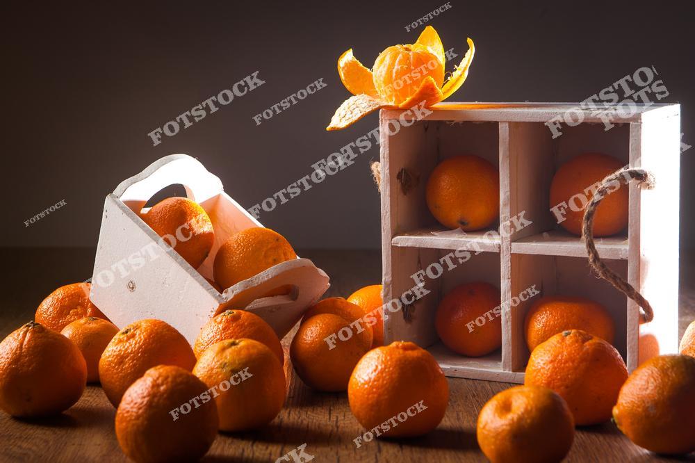На фотографии изображены сочные мандарины. Часть из них помещена в деревянные ящики, часть лежит на столе. Мягкое  освещение и теплые тона создают приятное настроение.